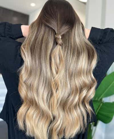 Special event balayage with soft warm tones and a seamless blend created by @hollydoesgreathair with Wella Professionals Blondor. Finished with a loose, half up style tied in a chic knot for an elevated look.